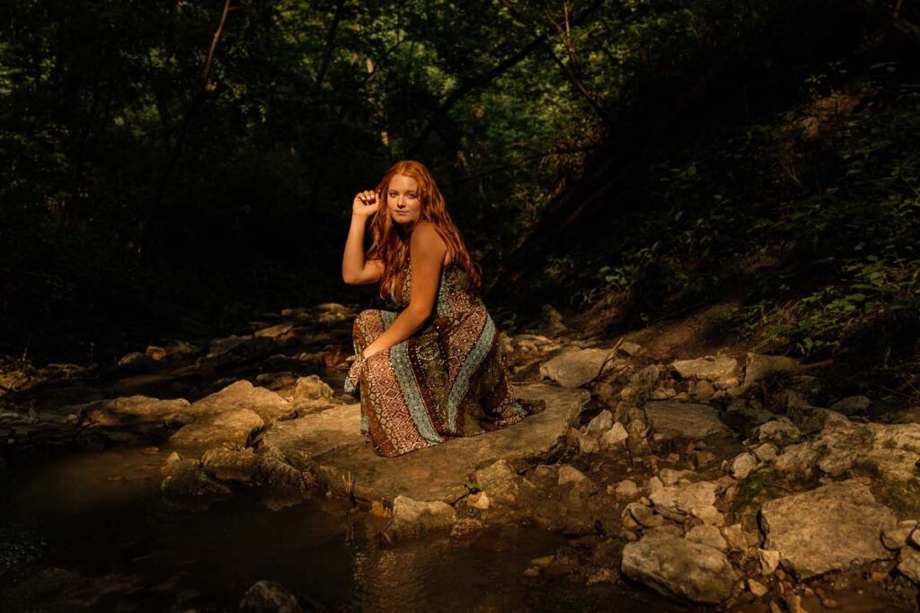 Senior girl in boho dress sitting on rocks by creek in Platte River State Park in Nebraska natural light photographer