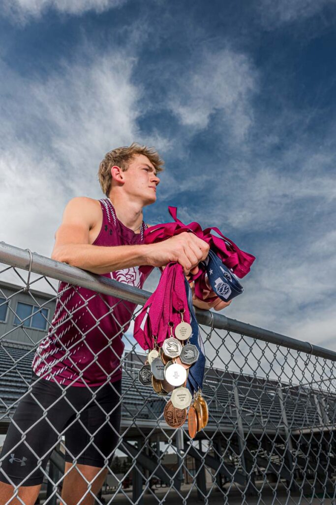 High school track athlete senior portrait with medals on fence Nebraska sports photographer