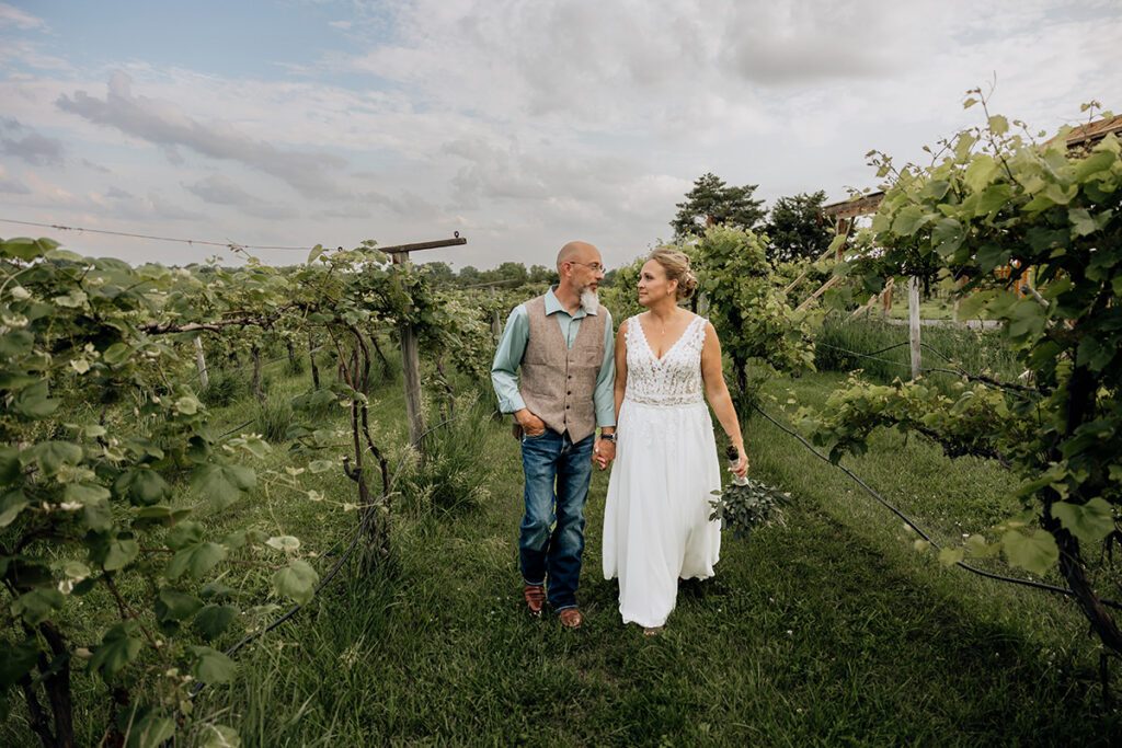 Bride and groom walking hand in hand through vineyard at Country Pines Lincoln Nebraska